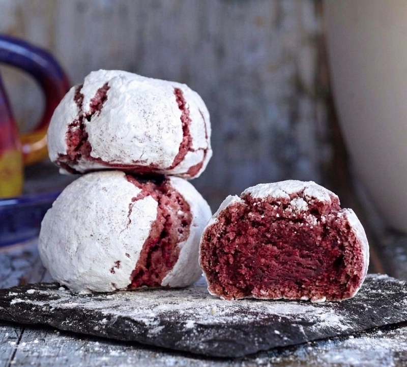 Red velvet cookies coated in white powdered sugar with cracked surfaces revealing deep red interiors.