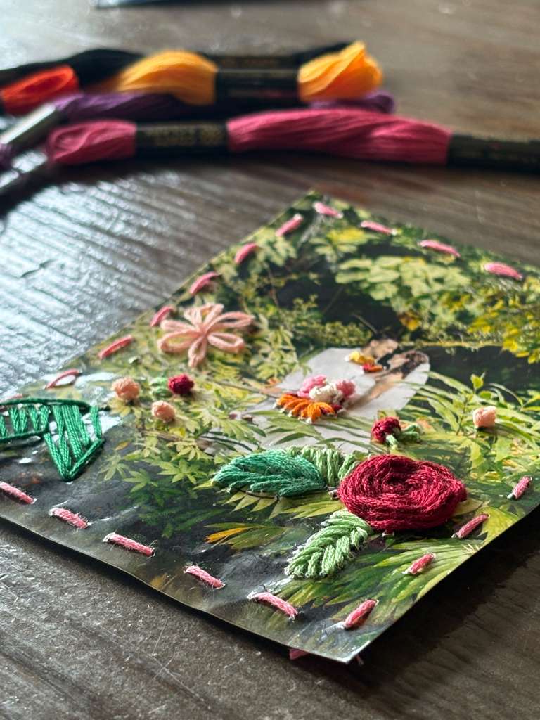 Embroidery hoop with colorful thread showing floral design in progress on fabric.