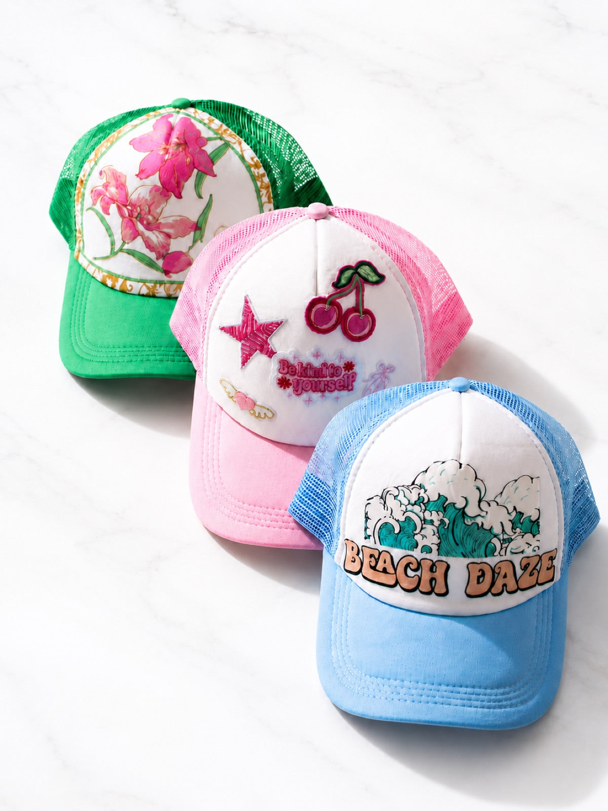Three finished custom trucker hats in green, pink and blue with embroidered and printed designs