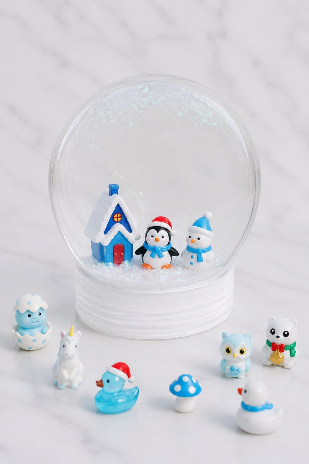 Finished snow globe holding a blue house and penguin, with spare figures around it