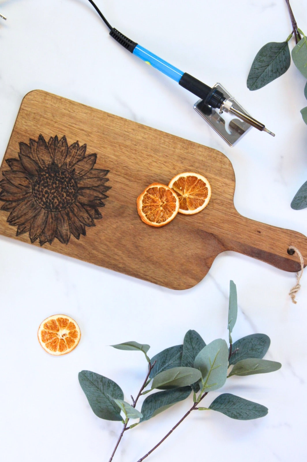 Wooden serving board with a burned sunflower design, dried orange slices and eucalyptus
