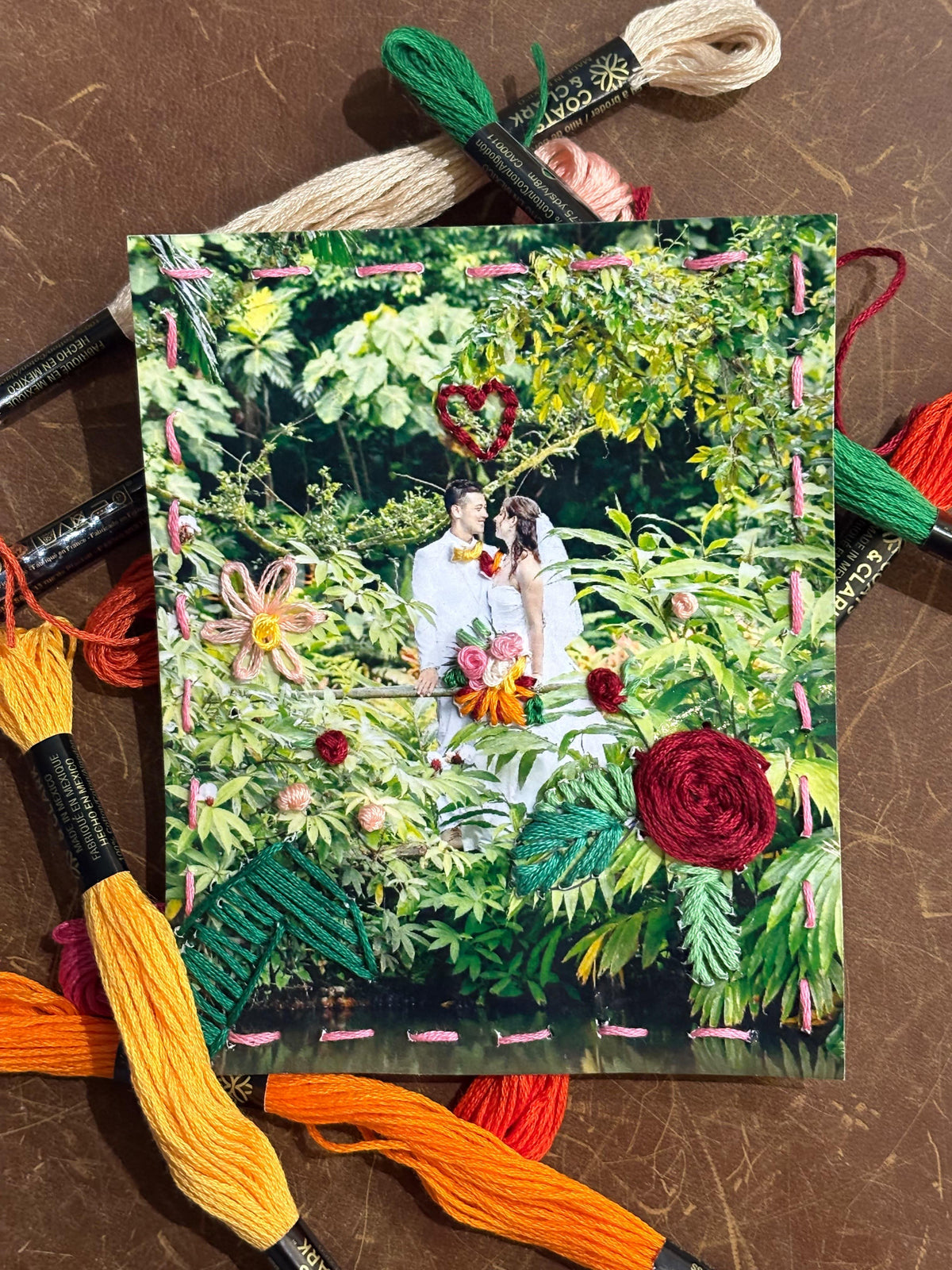 A wedding photo surrounded by embroidery floss in various colors on a brown surface.