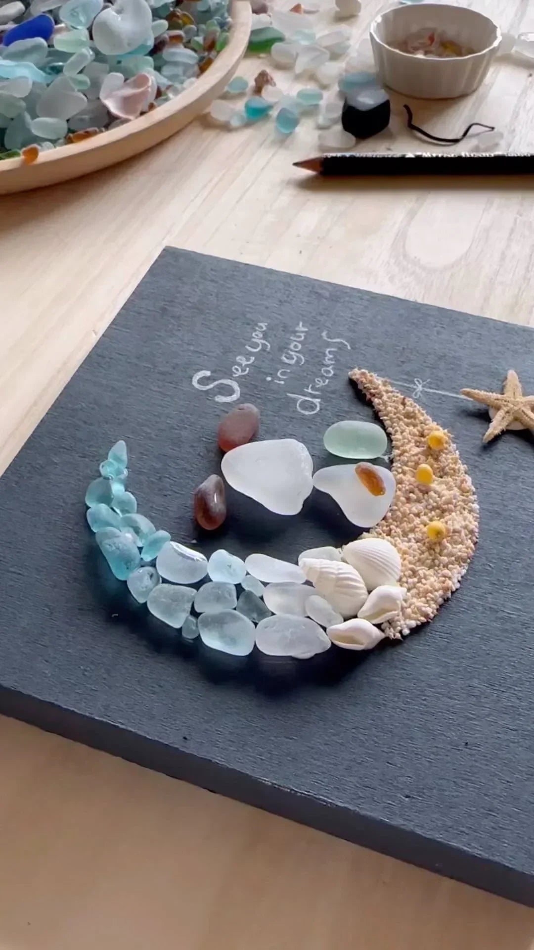 Decorative moon made of sea glass on a dark surface with 'See you in your dreams' text.