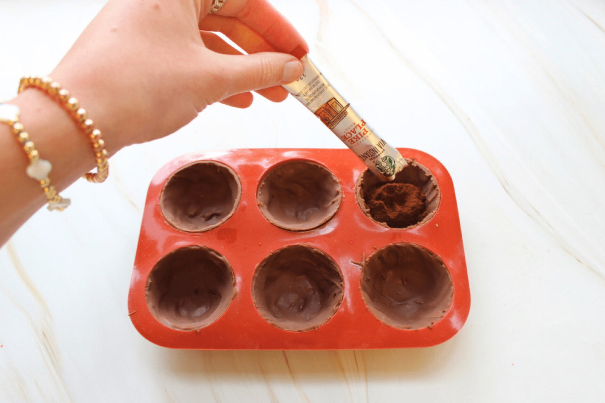 Hand brushing melted chocolate into the cups of a red silicone mould