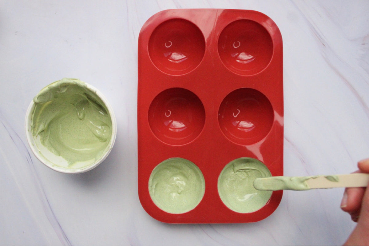 Spoon spreading green matcha white chocolate into a red silicone mould