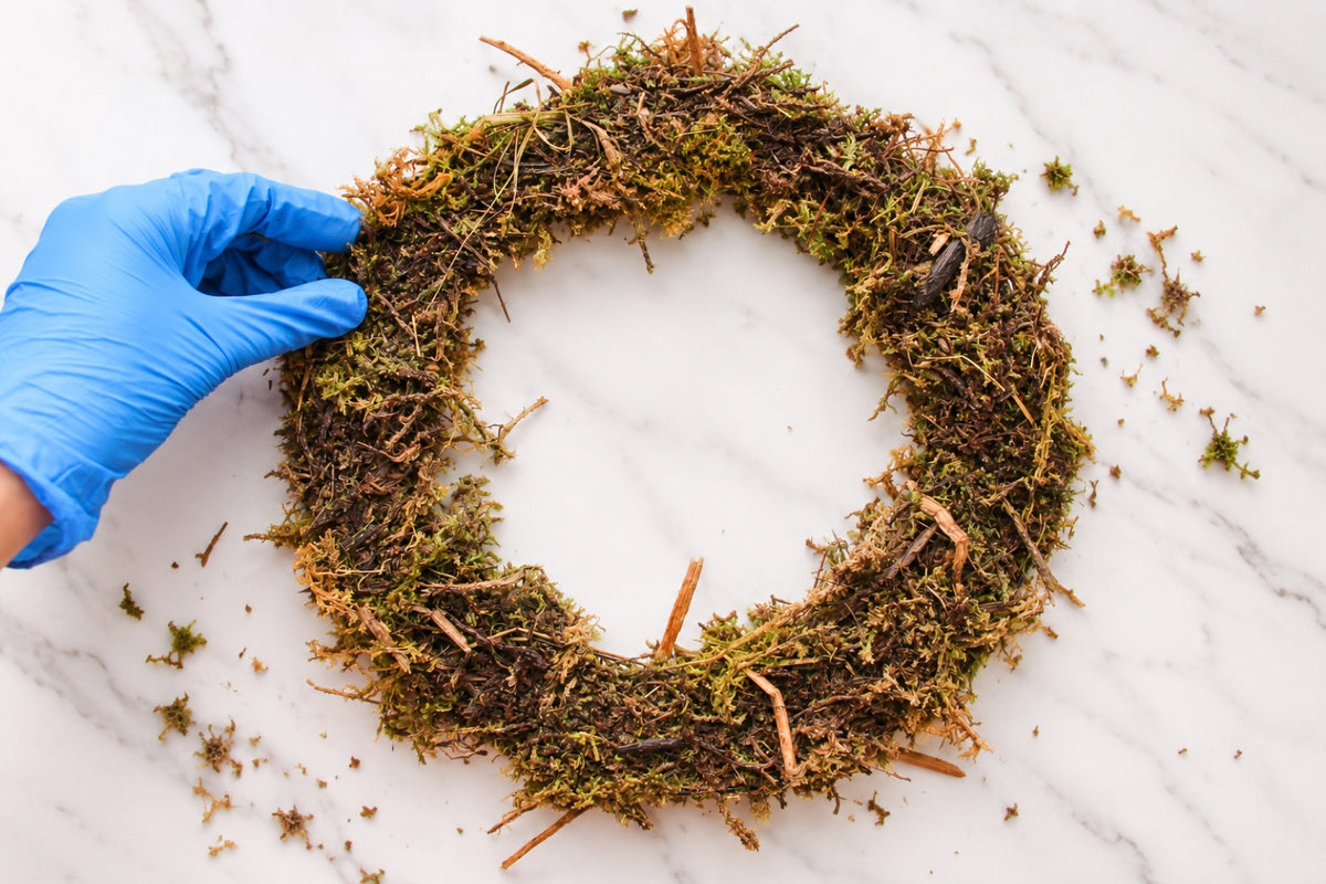 Gloved hand shaping a moss wreath base into a ring