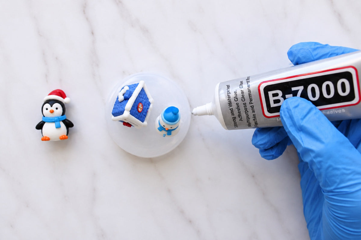 Gloved hand applying adhesive to figures on a snow globe base
