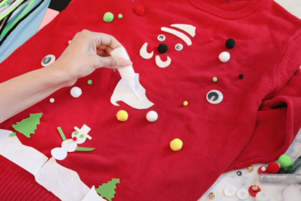 Hands arranging felt shapes on a red sweater before gluing