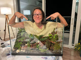 A woman pointing at a terrarium with houseplants inside.