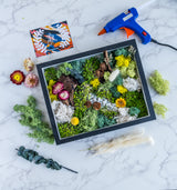 A picture frame with plants and flowers, accompanied by a blue and orange glue gun, suitable for arts and crafts projects.