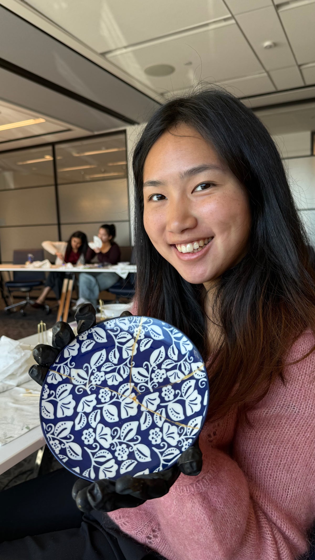 Woman holding a blue and white decorative ceramic plate while smiling in a workshop studio.