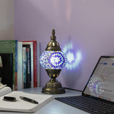 A decorative Turkish mosaic lamp with a colorful glass globe, providing ambient lighting on a desk with a laptop and other office supplies.