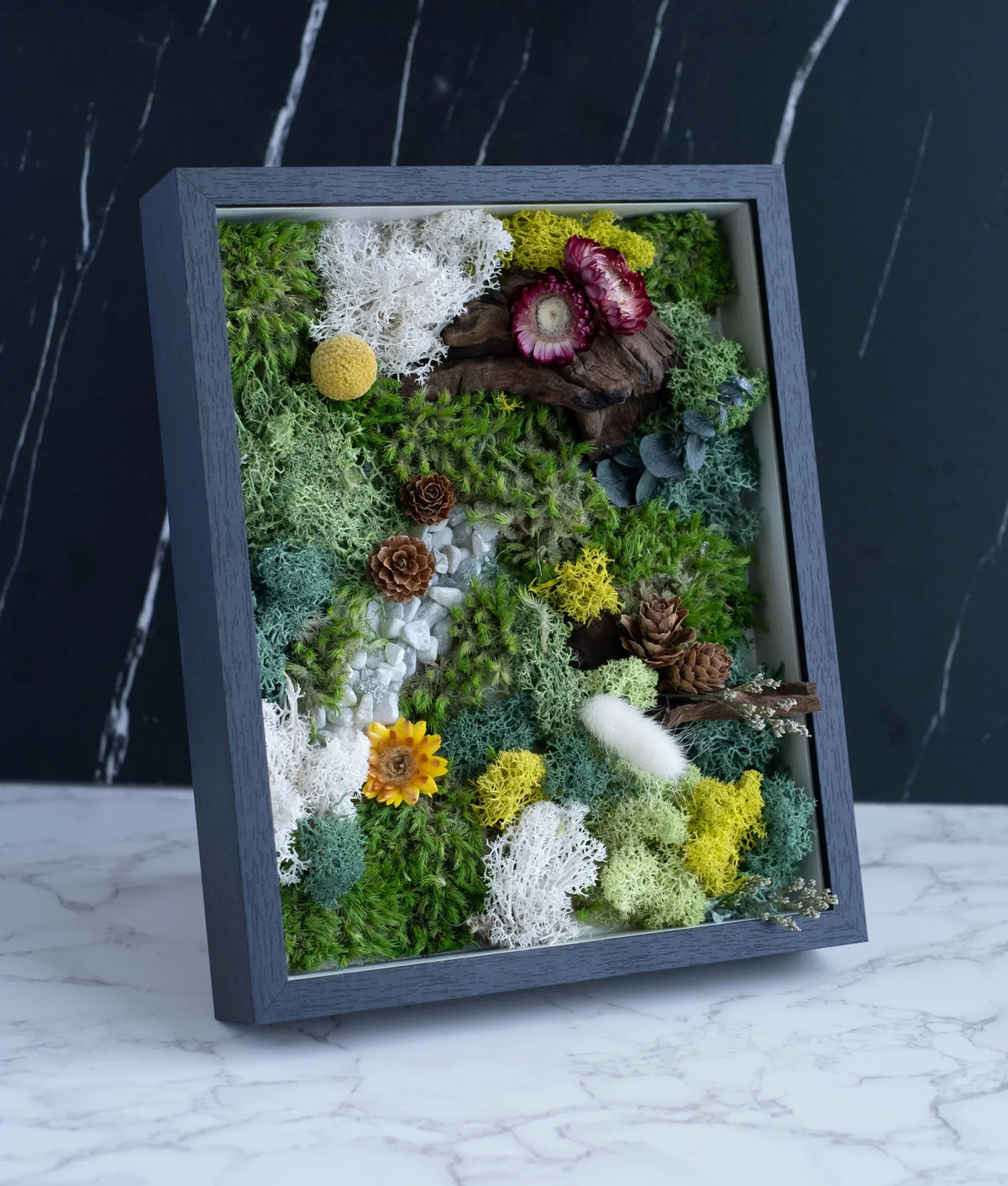 Framed moss wall art with preserved flowers, succulents, and white lichen in a gray wooden frame.