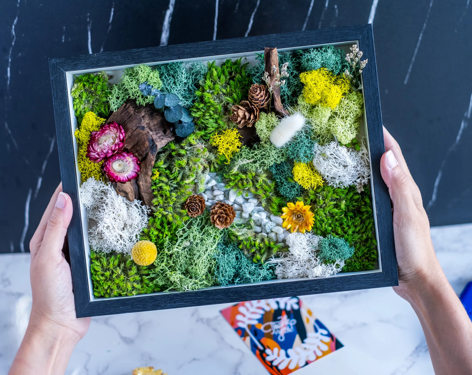 Guests displaying finished moss wall art pieces at a workshop in Austin, Texas