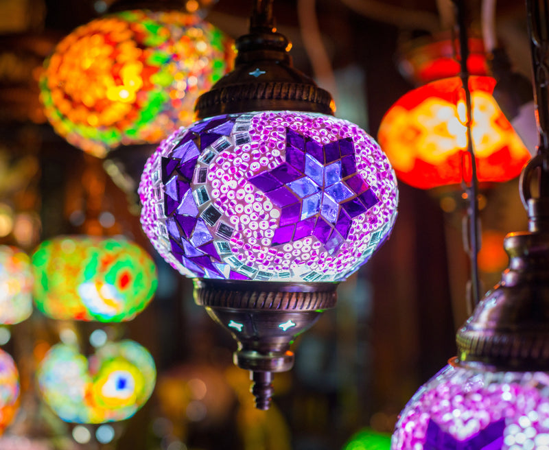 A participant assembles a structured geometric mosaic lamp using hand-cut glass tiles and a brass base.