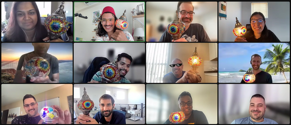 A vibrant grid showcases 12 participants in a virtual craft workshop video call, each proudly displaying a colorful, mosaic-patterned decorative piece. Smiles abound as they present their creations, set against diverse backdrops featuring serene beaches, cozy rooms, and imaginative abstract designs.